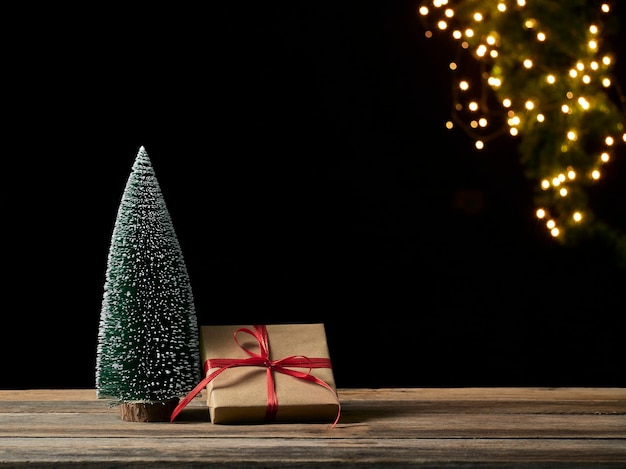 Contenitore di regalo di Natale e albero di abete sulla tavola di legno contro luci festive sfocate, spazio per testo