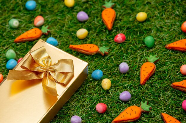 Contenitore di regalo dorato ed uova di Pasqua con le carote del biscotto sull'erba verde