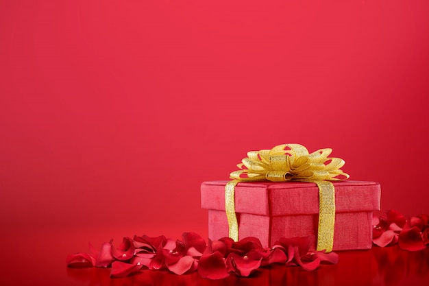 Contenitore di regalo e petali di rosa rossa su un fondo rosso