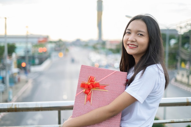 Contenitore di regalo felice della tenuta della giovane ragazza sul fondo di vista della città.