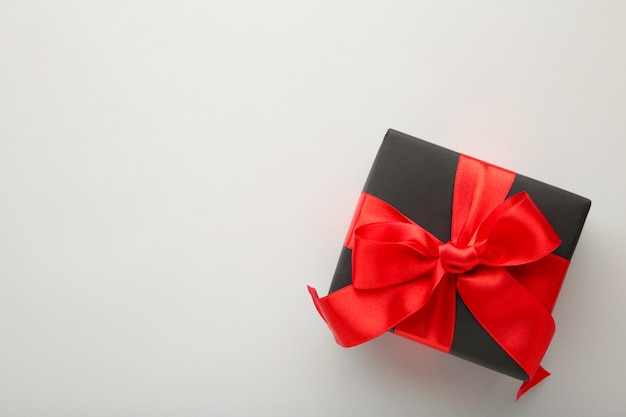 Contenitore di regalo nero con nastro rosso e fiocco su grigio.