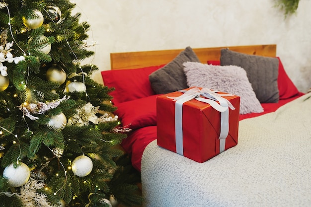 Contenitore di regalo rosso di Natale sul letto vicino all'albero a casa