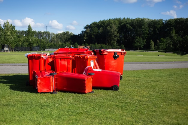 Contenitori di immondizia rossi sull'erba verde nel parco sulla superficie del cielo blu.