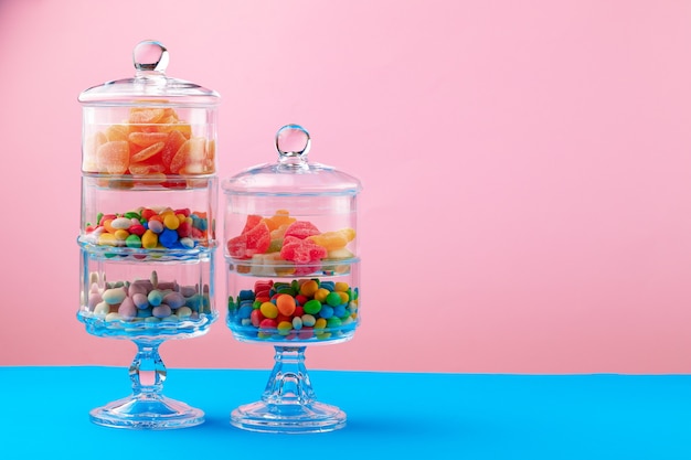 Contenitori di vetro con caramelle e dolci su sfondo rosa