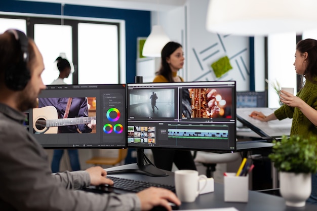 Contenuti del creatore che indossano le cuffie che modificano il montaggio del film nel software di post produzione sul computer con configurazione a doppio monitor