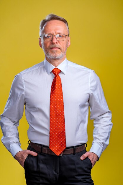 Contenuto uomo d'affari senior in camicia e gilet in posa in studio su sfondo giallo Concetto di stile business fiducioso