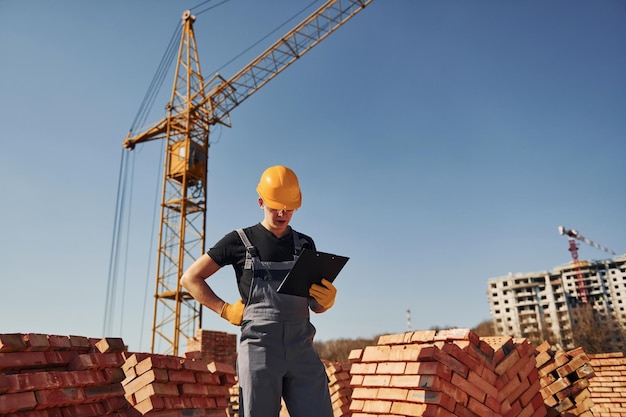 Contiene il blocco note con i documenti Il lavoratore edile in uniforme e le attrezzature di sicurezza hanno un lavoro sulla costruzione