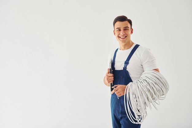 Contiene il blocco note dei cavi e il cacciavite Lavoratore maschio in uniforme blu in piedi all'interno dello studio su sfondo bianco