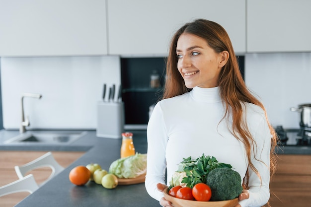 Contiene un piatto con verdure La giovane donna europea è al chiuso in cucina al chiuso con cibo sano