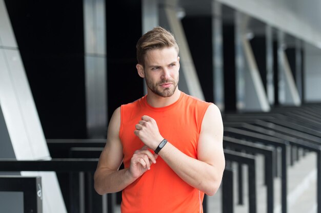 Continua a muoverti Allenamento sportivo con gadget contapassi allo stadio Concetto di gadget sportivo Atleta uomo faccia severa con attrezzature sportive sfondo urbano Fitness tracker o pedometro atleta