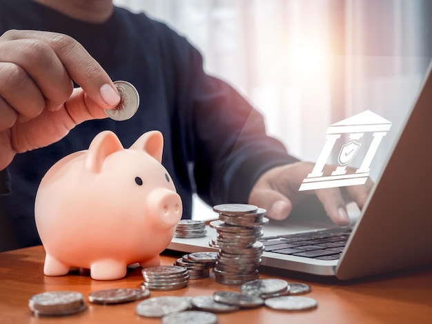 Conto di risparmio deposito online concetti di investimento finanziario digitale Icona di banca online che si mostra sullo schermo del computer portatile mentre l'uomo mette una moneta nella cassetta rosa vicino a molte pile di monete