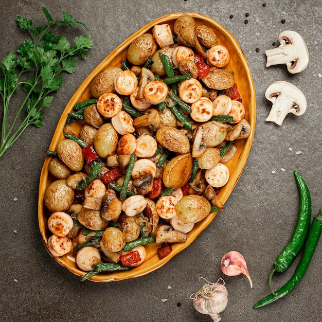 Contorno di verdure al forno asparagi fagioli, pepe, funghi e salsiccia, orientamento verticale. Sfondo di pietra grigia. Vista dall'alto