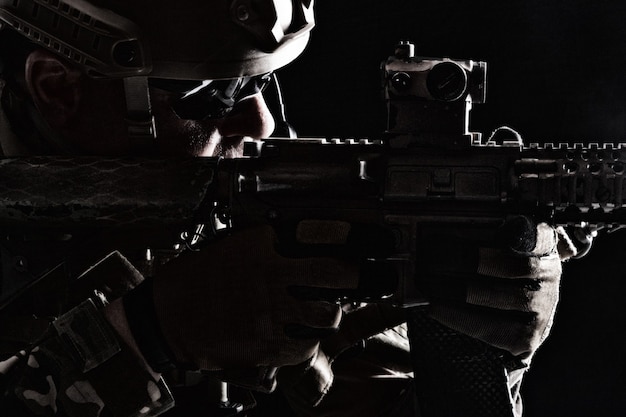 Contorno retroilluminazione ritratto di forze speciali soldato in uniforme che punta le armi, closeup ritratto su fondo nero