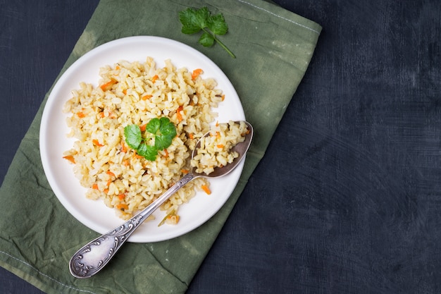 Contorno vegetariano stufato di riso integrale con cipolle e carote in una ciotola su un legno chiaro