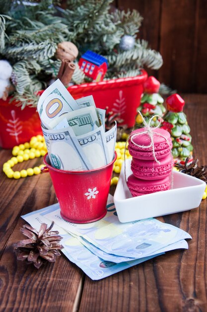 Contorto di banconote in dollari ed euro nel secchio di Natale rosso, euro e amaretti rosa