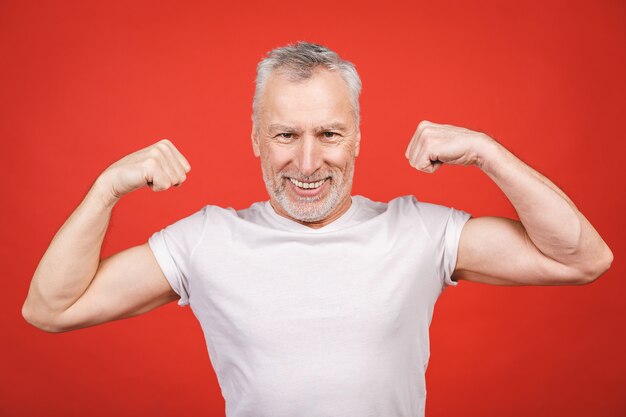 Controllalo! Uomo anziano che mostra i muscoli. Uomo invecchiato che flette le sue braccia isolate. Culturismo di pratica del nonno pensionato fresco moderno emozionante allegro.