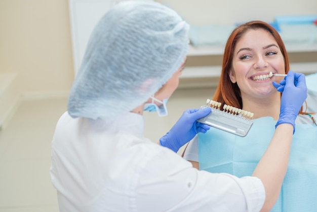 Controllare e selezionare il colore dei denti sulla poltrona del dentista Il dentista esegue il processo di trattamento di una bella ragazza dai capelli rossi Selezione di un impianto dentale