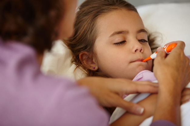 Controlliamo quella temperatura Inquadratura di una bambina sdraiata a letto mentre sua madre le misura la temperatura con un termometro