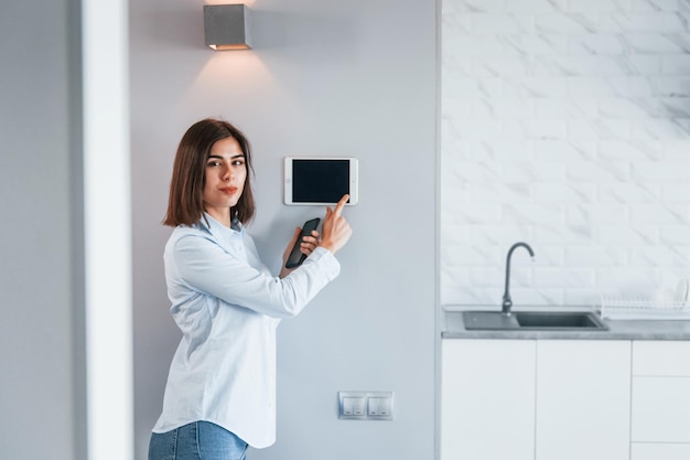 Controllo della casa con un solo tocco La giovane donna è al chiuso nella stanza della casa intelligente durante il giorno