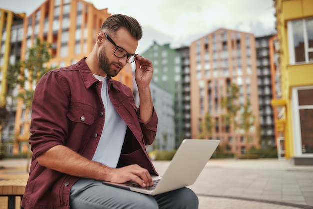 Controllo della posta elettronica giovane bell'uomo con la barba in abiti casual che si aggiusta gli occhiali e lavora su