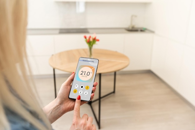 Controllo della temperatura, della sicurezza e dell'ambiente della casa su app mobile. Smart phone in mano di donna. Soggiorno sullo sfondo.