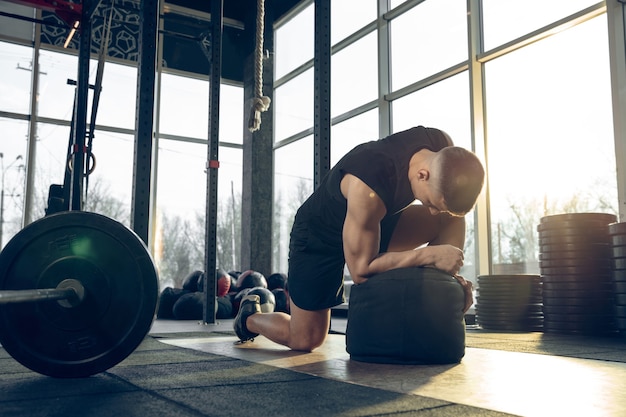 Controllo. Giovane atleta caucasico muscolare che si allena in palestra, fa esercizi di forza, pratica, lavora sulla parte superiore del corpo con pesi e palla. Fitness, benessere, sport, concetto di stile di vita sano.