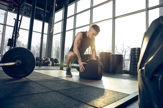 Controllo. Giovane atleta caucasico muscolare che si allena in palestra, fa esercizi di forza, pratica, lavora sulla parte superiore del corpo con pesi e palla. Fitness, benessere, sport, concetto di stile di vita sano.