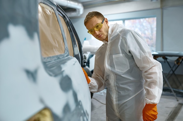 Controllo qualità nel servizio auto. Riparatore che controlla il lavoro finito. Rimozione e adescamento di vecchie pitture