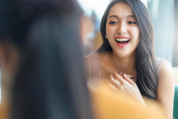 Conversazione di felicità femminile asiatica positiva attraente sorridente ridere cheeful parlando con un amico al ristorante caffetteria con luce naturale dal concetto di stile di vita casual della finestra