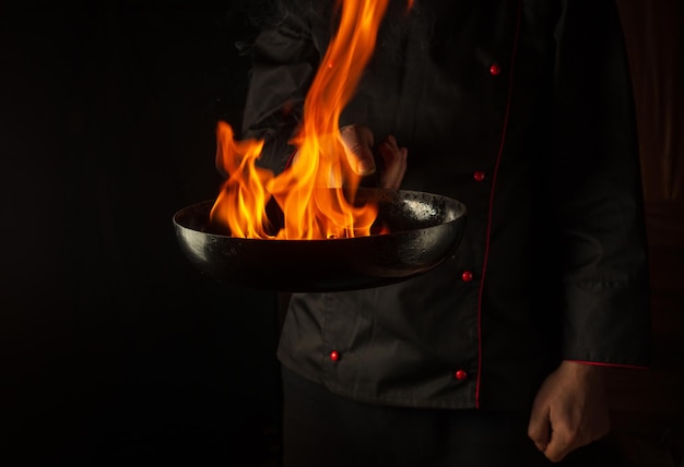 Cook prepara il cibo vegetale in una padella con una fiamma di fuoco