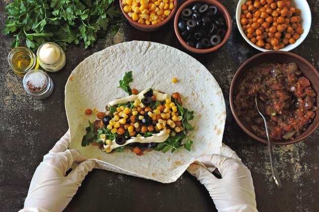 Cooking shaanma vegan. Le mani nei guanti da cucina impongono un ripieno di pane pita per preparare lo shawarma. Cucina mediorientale.