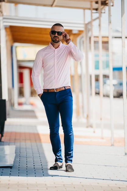 Cool bell'uomo caucasico che indossa un'elegante camicia rosa chiaro e occhiali da sole in posa all'aperto