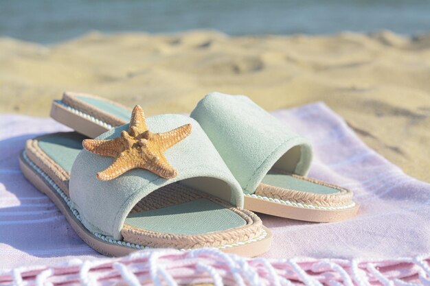 Coperta rosa con eleganti pantofole e stelle marine asciutte sulla spiaggia sabbiosa vicino al primo piano del mare