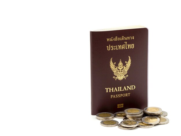 Copertura del passaporto della Tailandia, cittadino di identificazione con le monete isolate su fondo bianco.