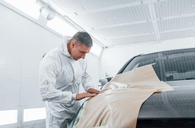 Copertura dell'auto con un panno marrone Il riparatore di automobili caucasico in uniforme lavora in garage