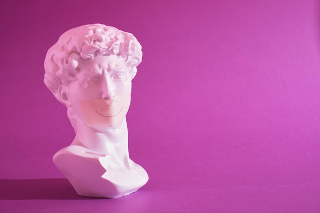 Copia della testa di un'antica statua del David con la bocca nastrata in luce al neon rosa su sfondo viola