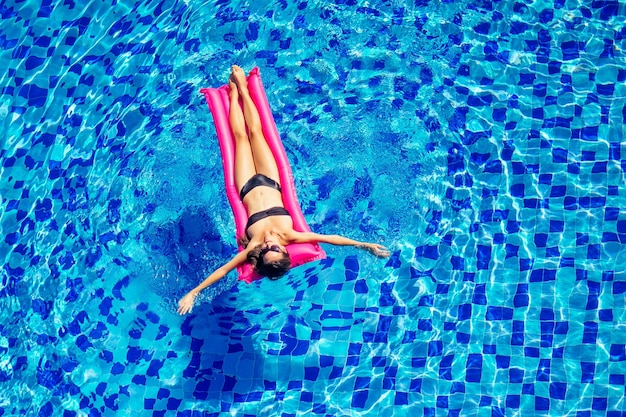 Copia spazio spf e crema solare bella ragazza bruna che galleggia nella piscina waterwoman che nuota e si rilassa sul materasso gonfiabile rosa in piscina blu lavoro a distanza e freelance