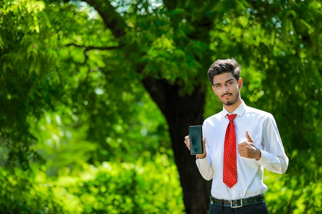 Copia spazio sul suo smart phone. Fiducioso giovane indiano che mostra il suo smart phone