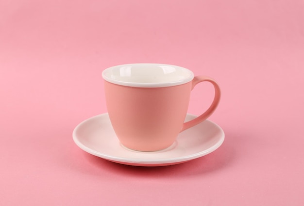 Coppa e piattino di ceramica vuoti su sfondo rosa