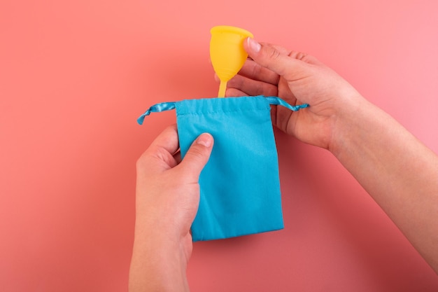Coppa mestruale in silicone giallo con custodia blu igiene alternativa per le mani femminili su sfondo rosa