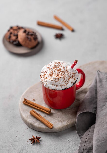Coppa rossa di cacao caldo o cioccolato con panna montata e biscotti bastoncini di cannella su uno sfondo grigio