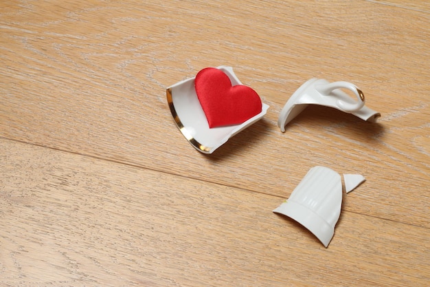 Coppa rotta sul pavimento Coppa e cuore rosso su uno sfondo di legno Concetto di amore cuore spezzato