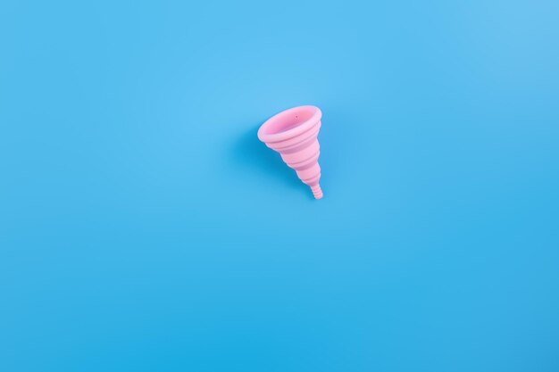 Coppetta mestruale rosa in silicone Salute delle donne e igiene alternativa su fondo blu piatto