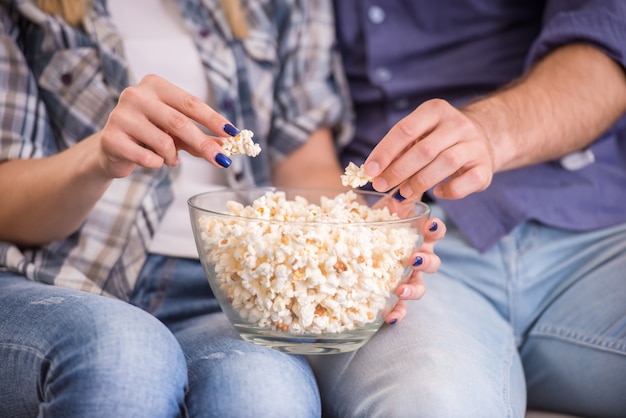 Coppia a casa seduto sul divano, guarda la TV e mangia popcorn.