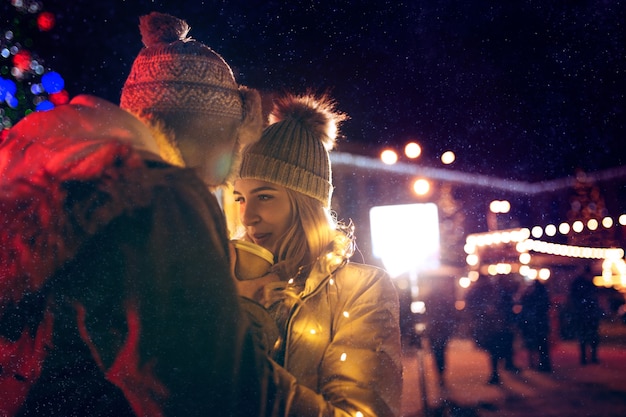 Coppia adulta in giro per la città durante il periodo natalizio sullo sfondo delle luci della città e la neve di notte