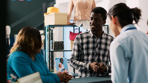 Coppia afro-americana che prende una scatola di cartone con vestiti alla moda, in piedi al bancone del negozio in una moderna boutique. Clienti che discutono del prezzo dell'ordine online con un dipendente elegante. concetto di moda