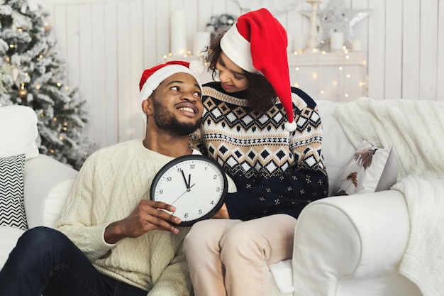 Coppia afro-americana che si guarda l'un l'altro, tiene in mano l'orologio che mostra cinque minuti al nuovo anno, copia spazio