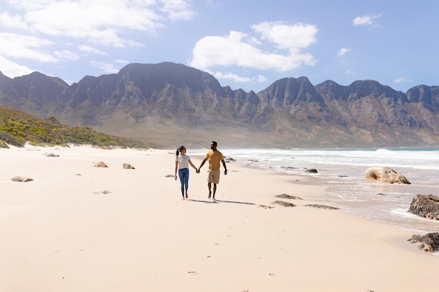 Coppia afroamericana che cammina tenendosi per mano su una spiaggia in riva al mare. stile di vita sano, tempo libero nella natura.