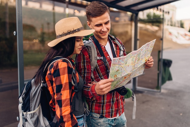 Coppia alla fermata dell'autobus studia la mappa delle attrazioni della città, escursione in località turistica. Escursioni estive. Escursione all'avventura di un giovane uomo e una donna