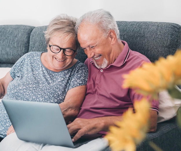 Coppia anziana anziana che usa insieme un computer portatile seduto sul divano navigando sul web Alla ricerca di attività di concetto di pagine internet web con uomo e donna maturi che si divertono e godono della tecnologia